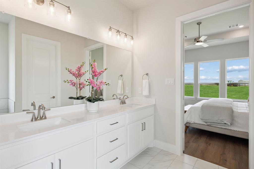 Dual-sink vanity with white cabinetry, light-toned countertop, and chrome fixtures, illuminated by multi-bulb vanity lighting