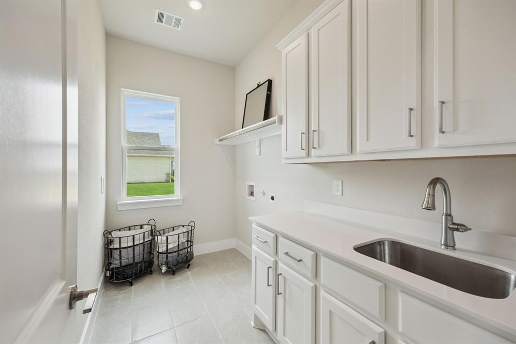 Utility space featuring white shaker-style cabinetry, a light-toned solid surface countertop, an undermount stainless steel sink with a high-arc faucet, and light-toned ceramic tile flooring