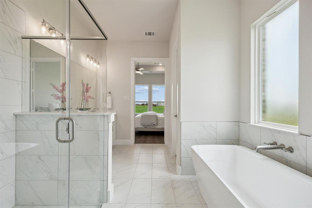 Bathroom featuring a glass-enclosed shower with stone-finish wall tile, a deep soaking tub with a wall-mounted faucet, and tile flooring
