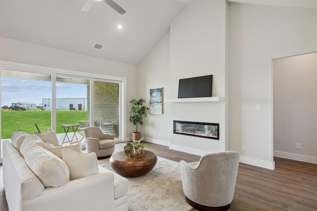 Modern living room featuring a linear fireplace with integrated media niche, wood-finish flooring, and expansive glass doors opening to a manicured lawn