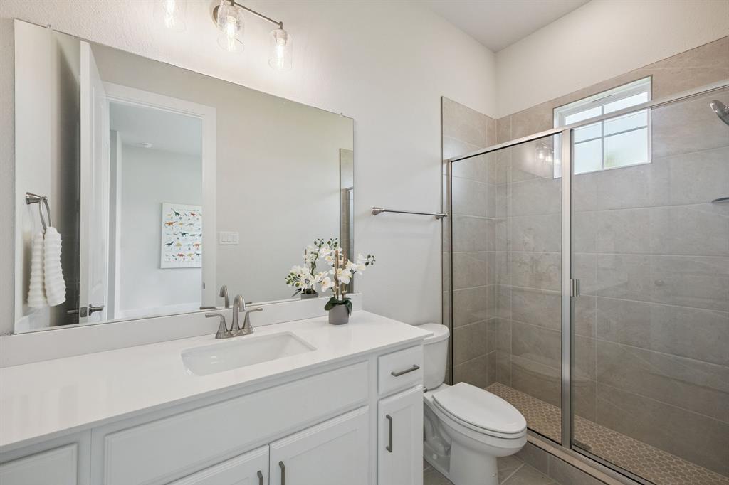 Bathroom featuring a white vanity with a light-toned countertop, large wall-mounted mirror, three-light fixture, and a glass-enclosed shower with tile surround
