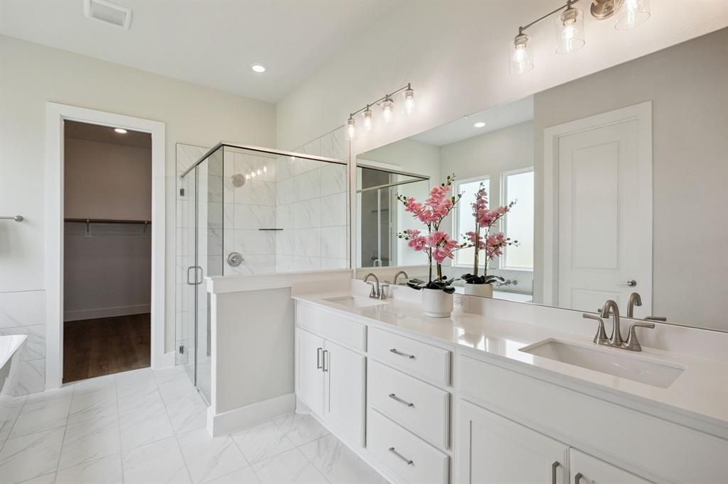 Dual-sink vanity with quartz countertop, walk-in glass-enclosed shower featuring tiled surround, and expansive wall-mounted mirror