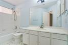 Bathroom featuring a white vanity cabinet, solid-surface countertop with an integrated sink, large wall-mounted mirror, and a tub-shower combination with a chrome showerhead