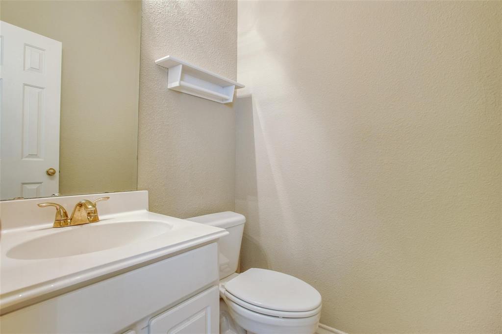 Single-sink vanity with a solid-surface countertop, gold-tone faucet, wall-mounted storage shelf, and neutral wall finish