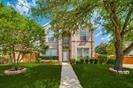 Two-story brick exterior featuring a multi-gabled roofline, arched window detailing, and a concrete walkway leading to the front entrance, complemented by mature trees and manicured lawn