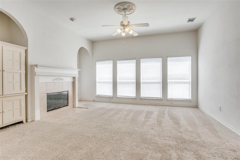High-ceilinged room featuring a fireplace with a mantel, built-in cabinetry, four tall windows with blinds, and a ceiling fan with a decorative medallion