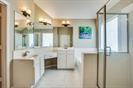 Bathroom featuring a dual-sink vanity with white cabinetry, a large wall-mounted mirror, light fixtures, and a glass-enclosed shower