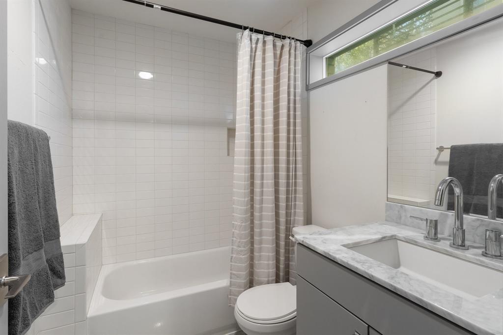 Bathroom featuring a vanity with stone countertop and integrated sink, chrome widespread faucet, horizontal clerestory window, and tub enclosure with white tile surround