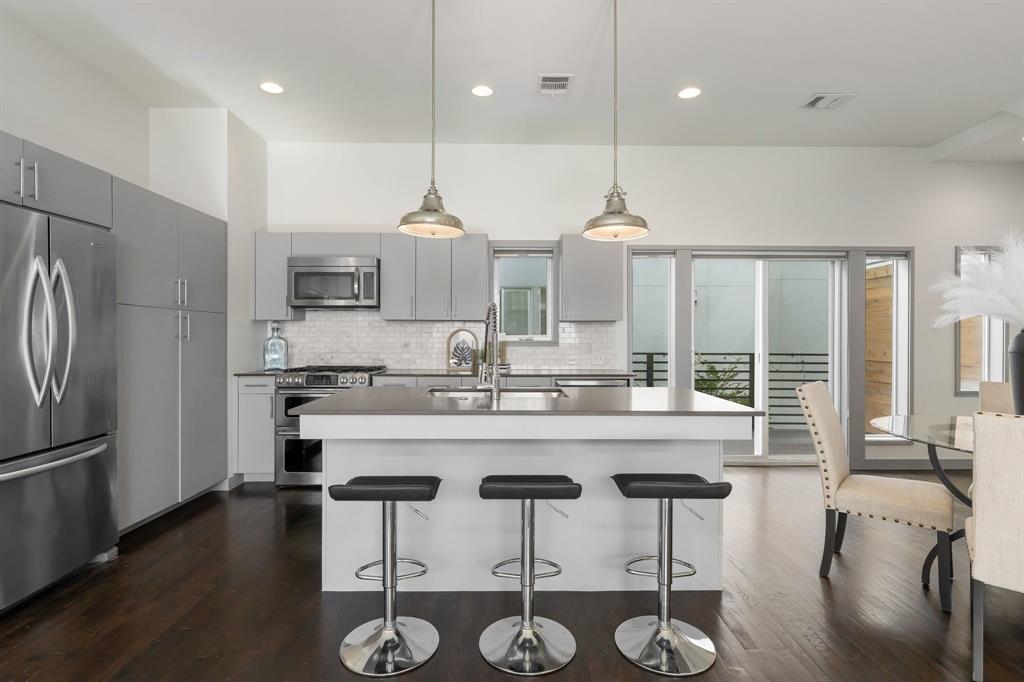 Kitchen featuring flat-panel cabinetry, a central island with a solid surface countertop, stainless steel appliances, white subway tile backsplash, and wood-finish flooring