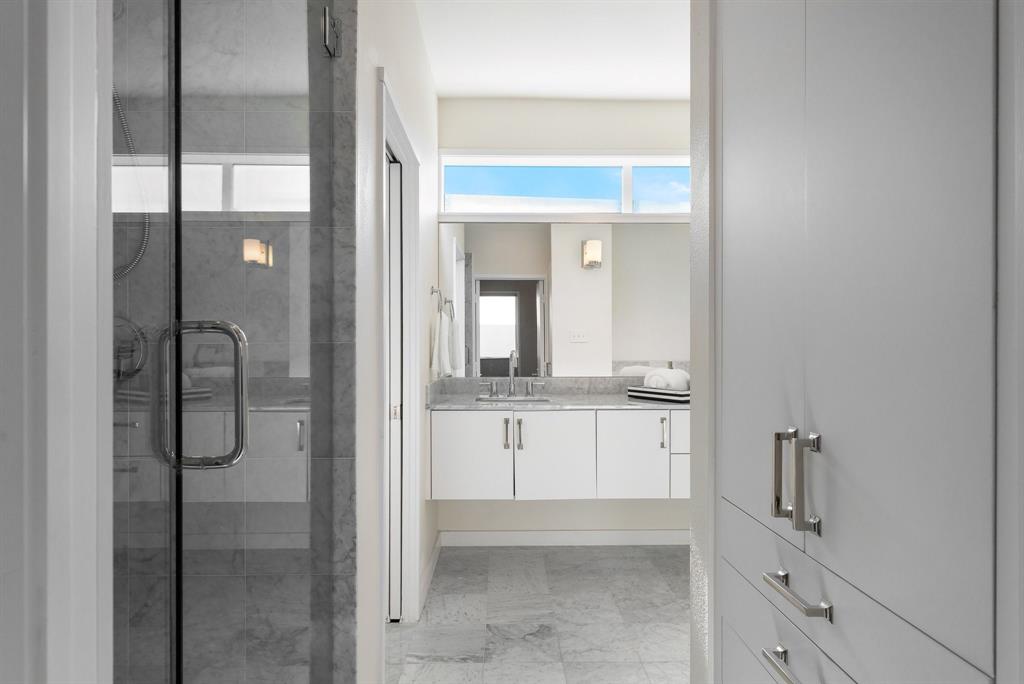 Floating vanity with stone countertop, glass-enclosed shower, built-in cabinetry, stone flooring, and clerestory windows