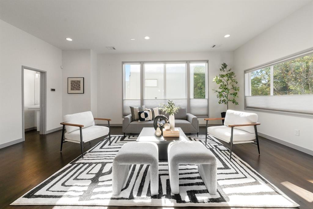 Living area featuring wood-finish flooring, recessed lighting, and large picture windows with horizontal shades