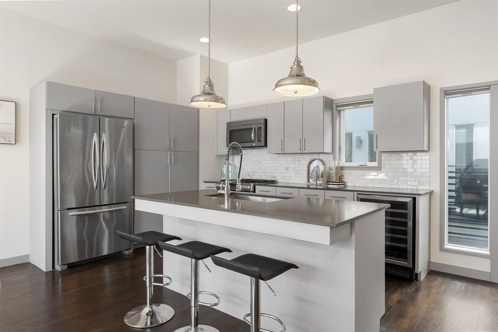 Kitchen featuring grey cabinetry, stone countertops, stainless steel appliances, subway tile backsplash, and dual industrial-style pendant lighting
