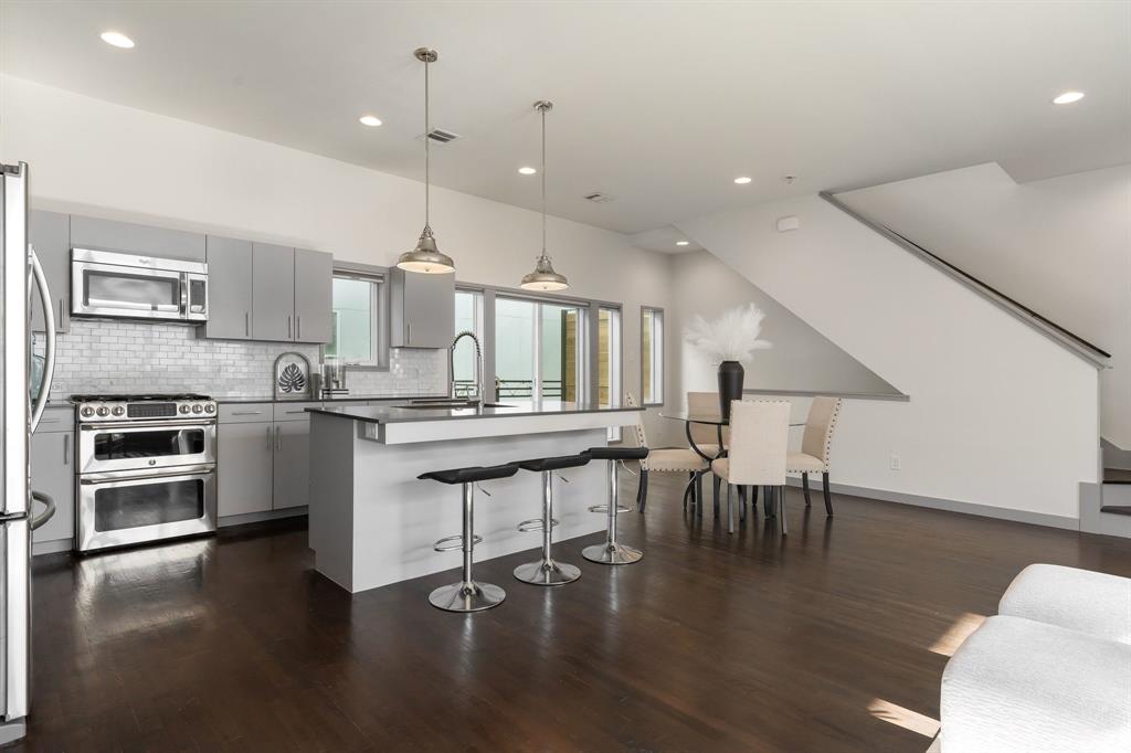 Modern kitchen featuring flat-panel cabinetry, stainless steel appliances, a tile backsplash, wood-finish flooring, and a center island with pendant lighting