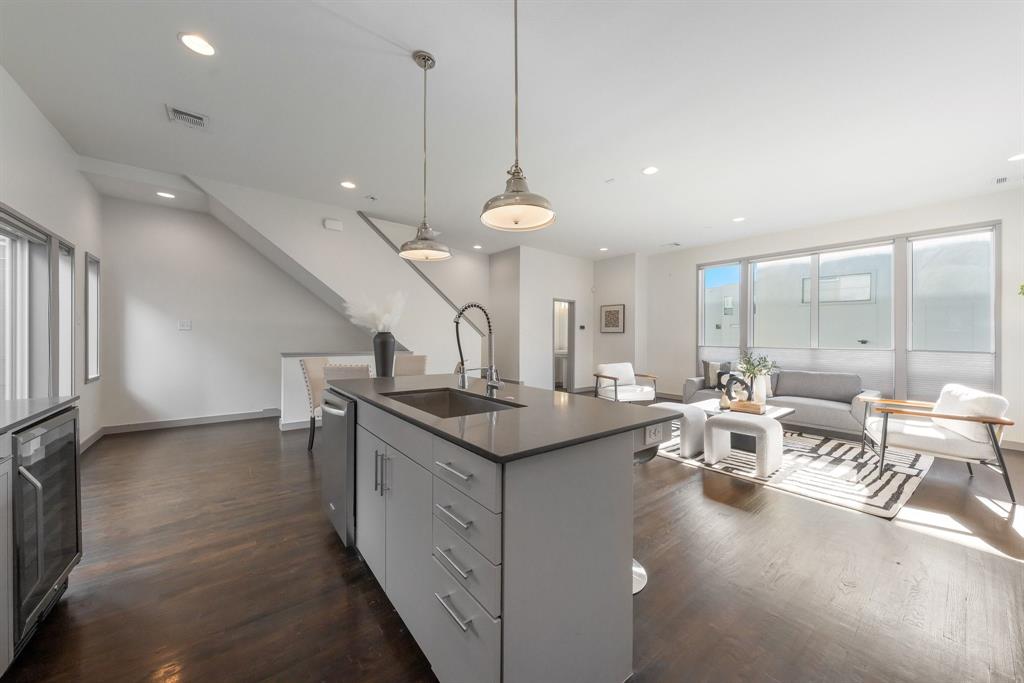 Open-concept kitchen featuring an island with a stone-composite countertop, stainless steel undermount sink, and high-arc faucet, complemented by wood-finish flooring and pendant lighting