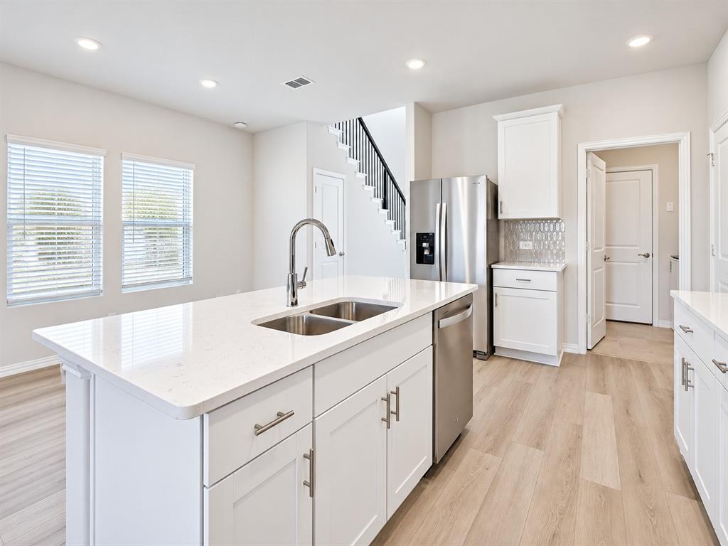 Modern kitchen featuring a large center island with dual sinks, white shaker cabinetry, stainless steel appliances, and wood-finish flooring