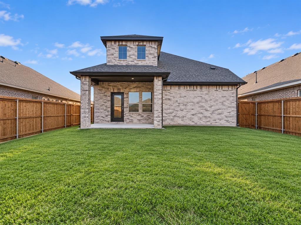 Expansive backyard featuring a manicured lawn, full privacy fencing, and a covered patio