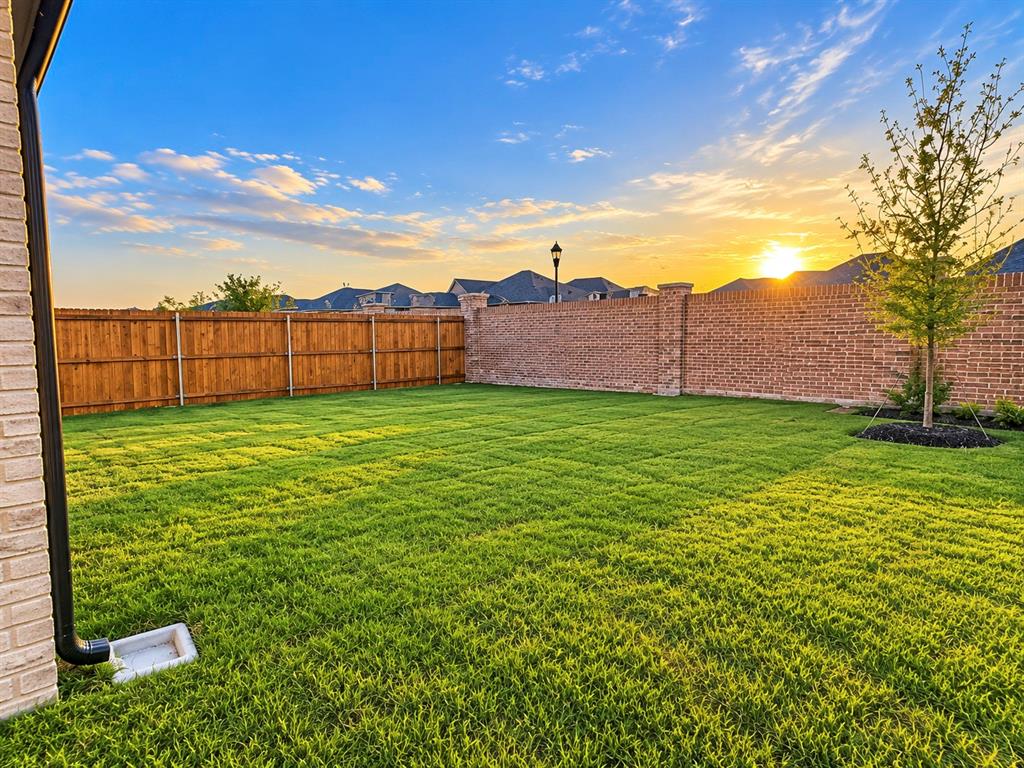 Expansive rear yard featuring green lawn, brick perimeter wall, and wood fencing