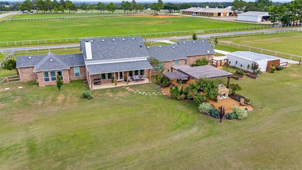 Brick exterior residence with a covered patio, detached storage building, wood pergola, and outdoor masonry fireplace situated on a large tract of land with white perimeter fencing