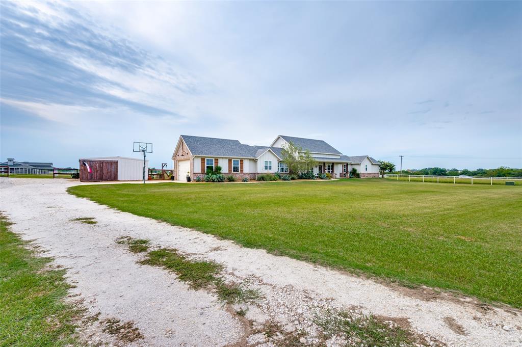 Exterior featuring a multi-gabled roofline, stone and siding facade, extensive grassy acreage, and a gravel driveway
