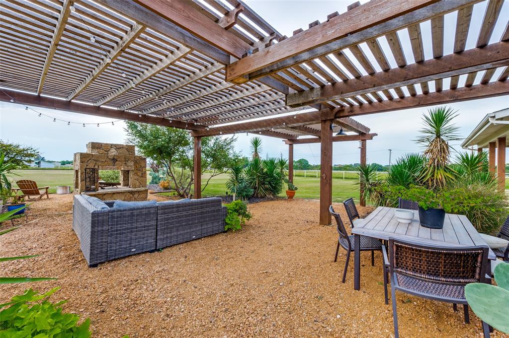 Outdoor patio area featuring a stained timber pergola, natural stone outdoor fireplace, and crushed gravel ground cover