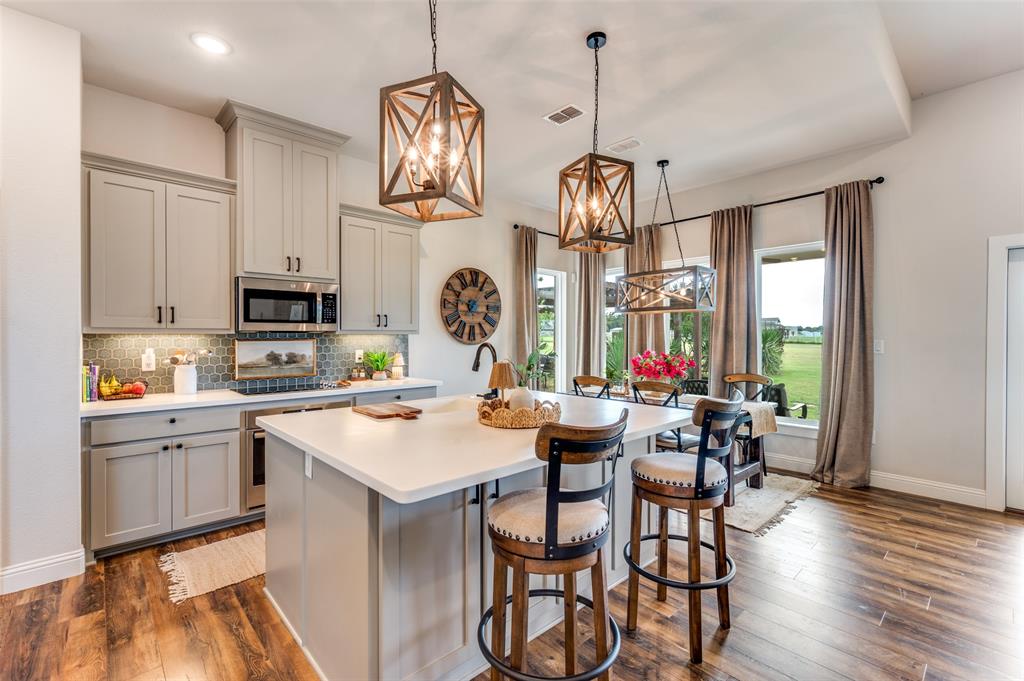 Kitchen featuring custom cabinetry, a central island with a quartz countertop, geometric lantern-style pendant lighting, and wood-finish flooring