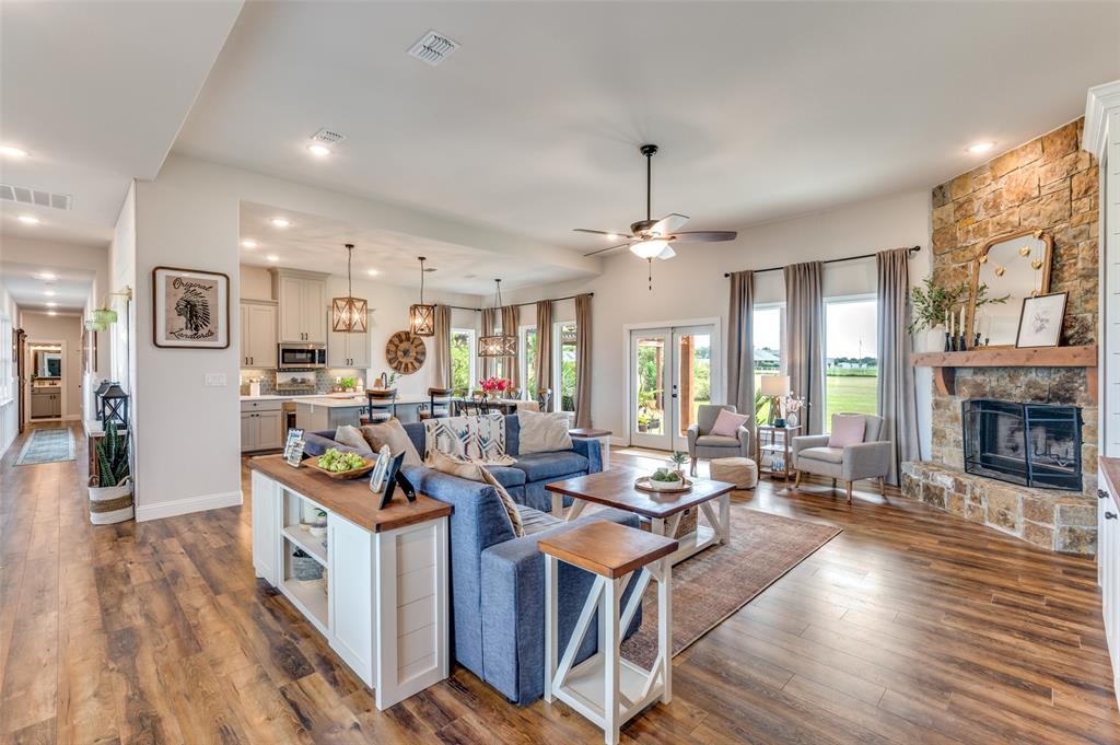 Open-concept interior featuring wood-finish flooring, a floor-to-ceiling stone fireplace with a wood mantel, recessed lighting, and a ceiling fan