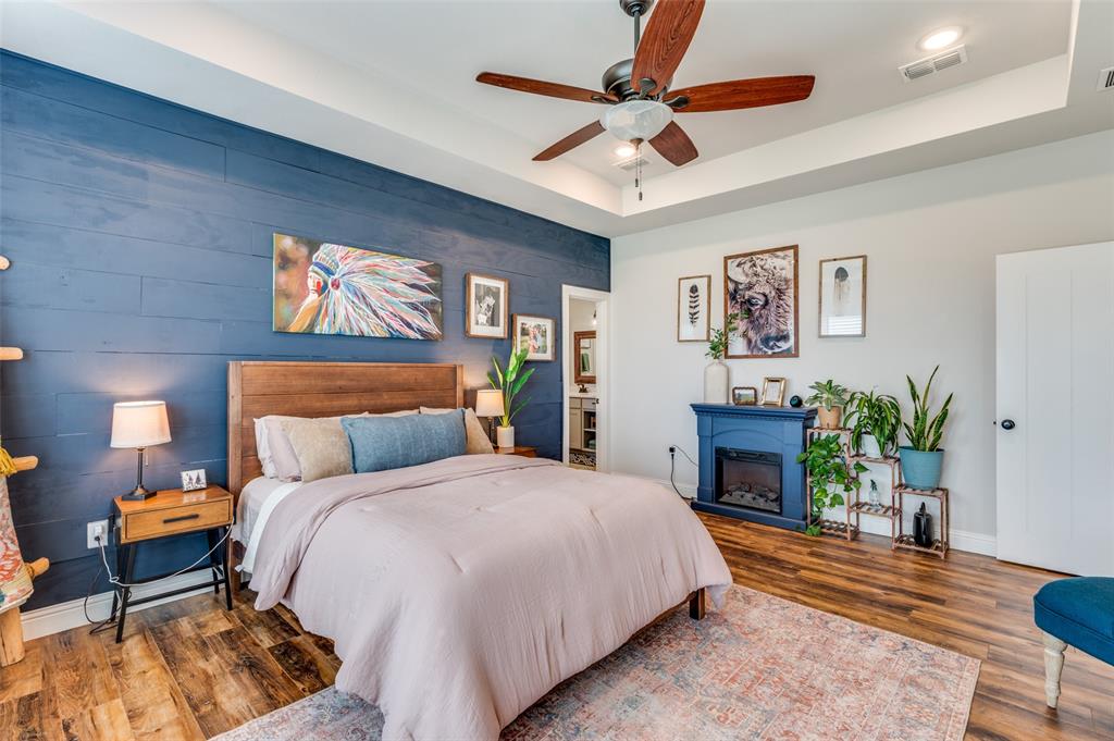 Wood-finish flooring, blue horizontal plank accent wall, tray ceiling with a multi-blade ceiling fan, and a built-in electric fireplace with a decorative mantel