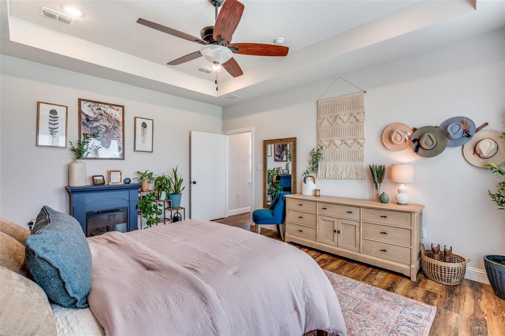 Tray ceiling, wood-finish flooring, ceiling fan with light fixture, and blue-painted built-in electric fireplace
