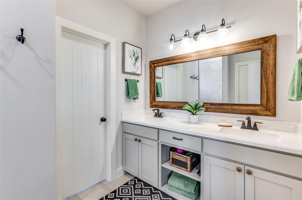 Dual-sink vanity with light-tone cabinetry, stone countertop, oil-rubbed bronze faucets, and a framed wall-to-wall mirror