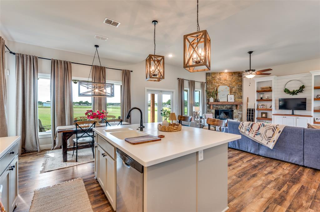 Kitchen island featuring a solid-surface countertop and a matte black faucet, open-concept layout with wood-finish flooring, stone-veneer fireplace with a wood mantel, and geometric lantern-style pendant lighting