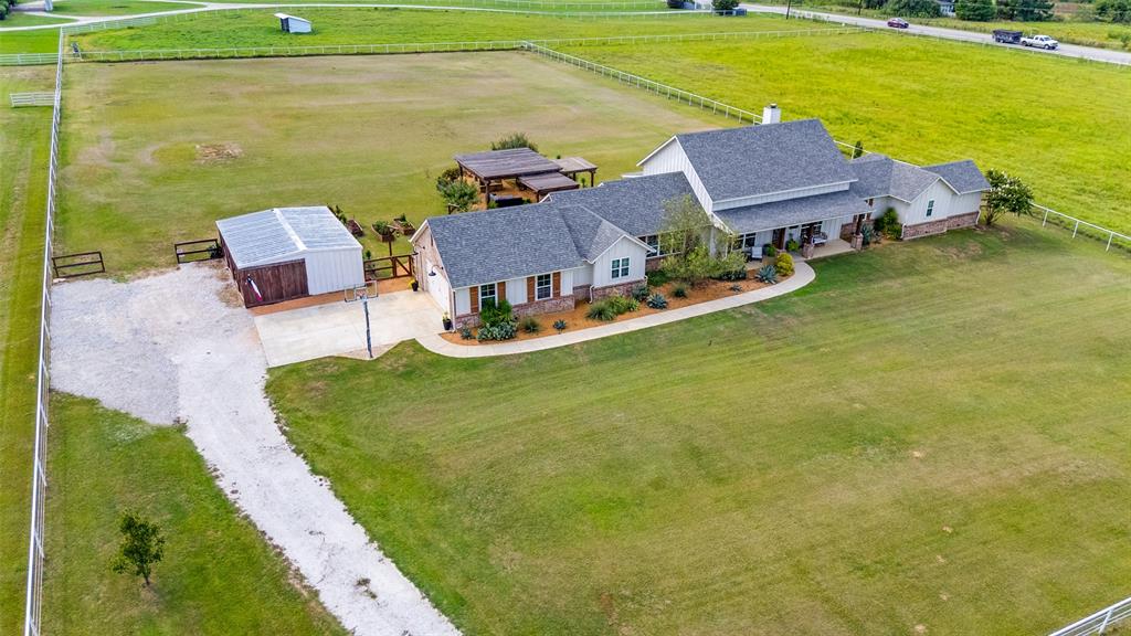 Aerial perspective of a multi-structure property featuring extensive acreage, a detached outbuilding, a covered outdoor pavilion, and concrete driveway