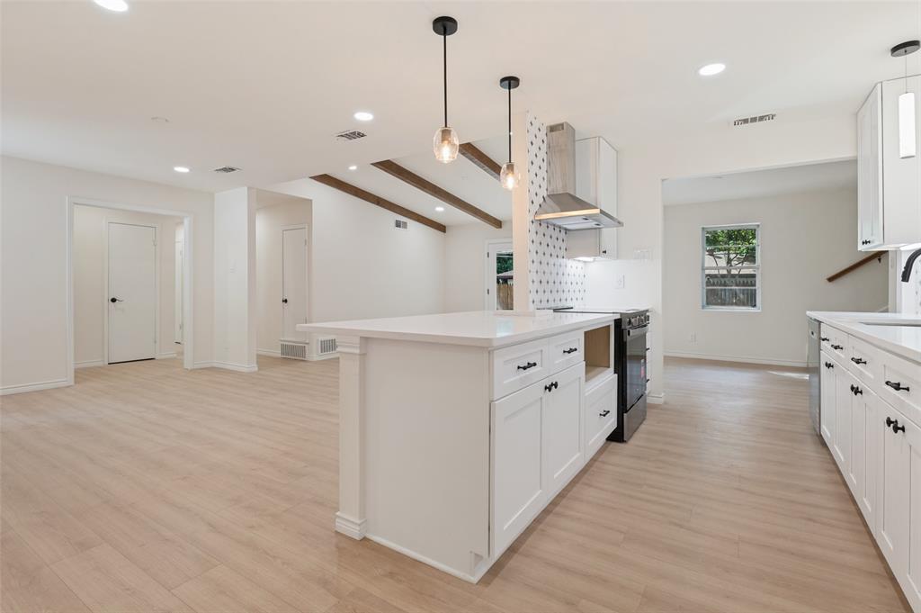 Kitchen featuring a central island with a solid-surface countertop, white shaker-style cabinetry, stainless steel range hood, patterned tile backsplash, and wood-finish flooring