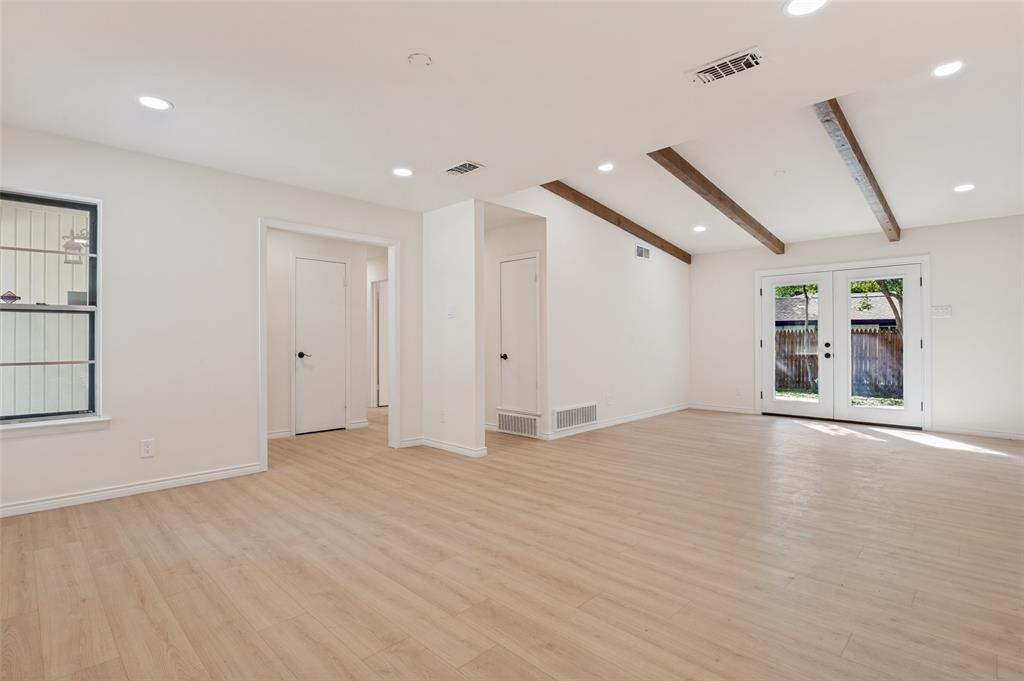 Open-concept interior featuring light-toned wood-finish flooring, exposed wooden ceiling beams, recessed lighting, and double glass-paned exterior doors
