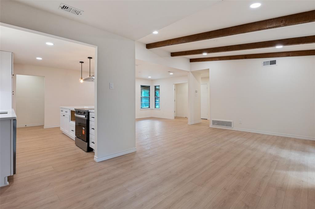 Open interior space featuring wood-finish flooring, exposed ceiling beams, recessed lighting, and kitchen cabinetry with a stainless steel range