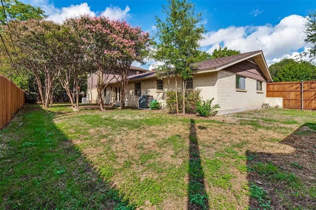 Exterior featuring a brick and horizontal siding façade, expansive lawn, mature shade trees, and wood privacy fencing