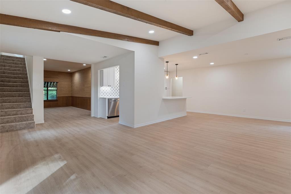 Open-concept interior featuring wood-finish flooring, exposed ceiling beams, recessed lighting, and a breakfast bar with dual pendant lights