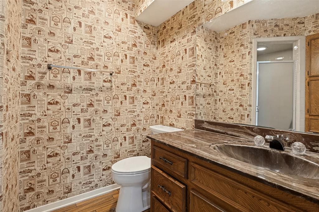 Bathroom featuring a stone-finish countertop with an integrated basin, wood cabinetry with metallic hardware, a wall-spanning mirror, and a towel bar