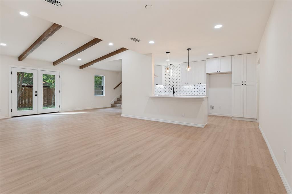 Open-concept space featuring wood-finish flooring, exposed ceiling beams, custom shaker-style cabinetry, a patterned tile backsplash, and recessed lighting