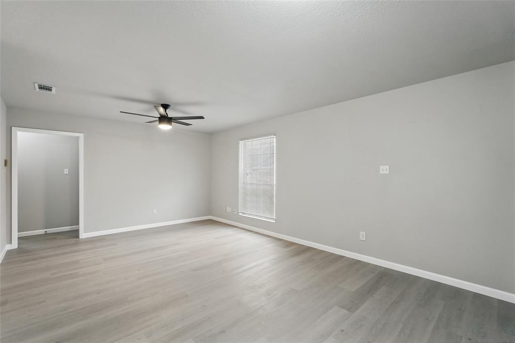 Spacious room featuring wood-finish flooring, neutral wall paint, and a ceiling-mounted light fixture with fan blades
