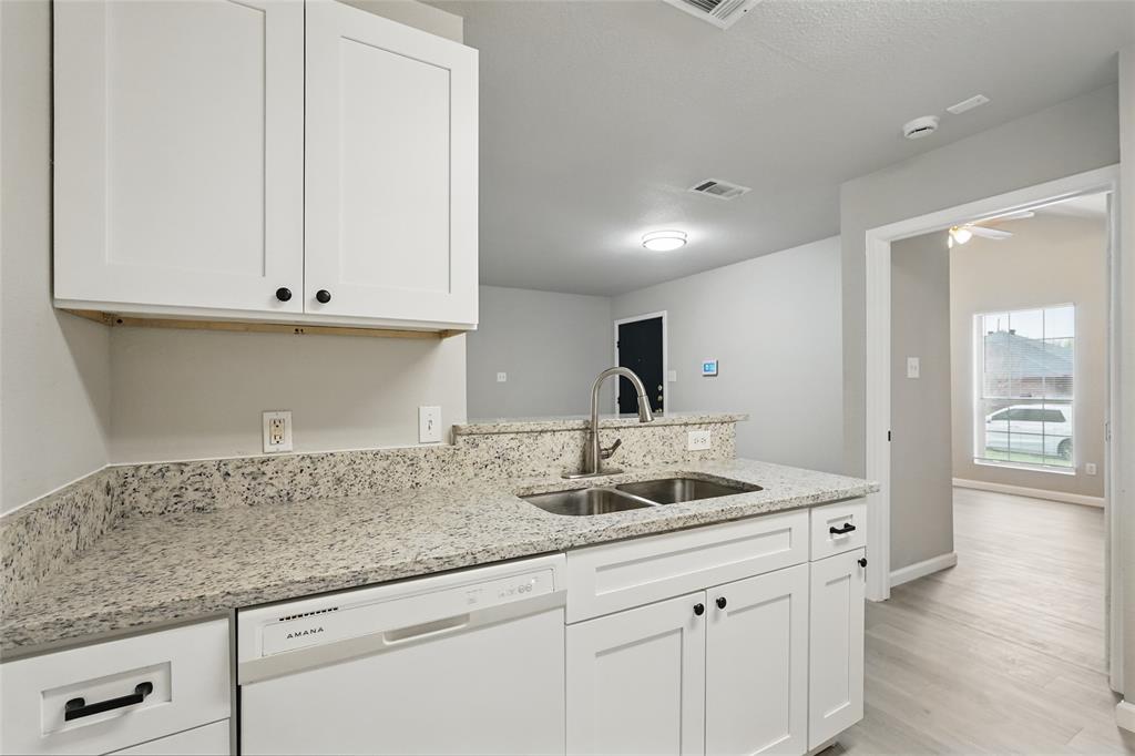 Kitchen featuring white shaker-style cabinetry, stone-finish countertops, stainless steel dual-basin sink, built-in dishwasher, and wood-finish flooring