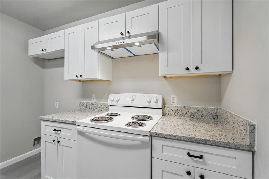 White shaker-style cabinetry, speckled stone-finish countertops, stainless steel range hood, and matte black hardware
