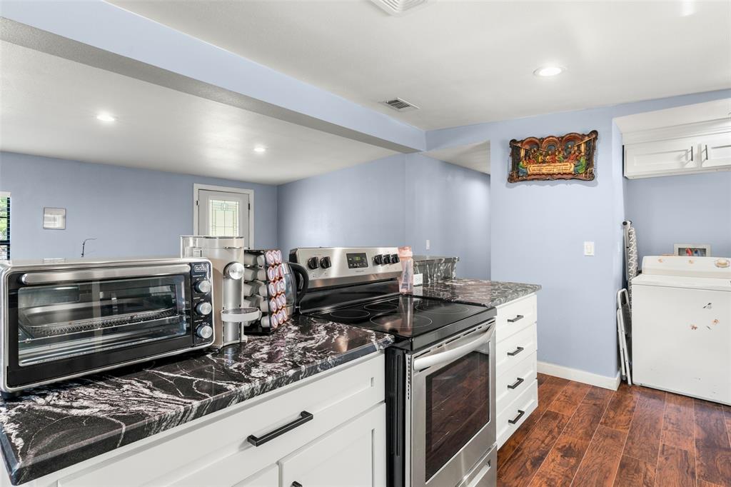 Kitchen featuring dark stone-patterned countertops, white shaker-style cabinetry with matte black hardware, stainless steel electric range, and wood-finish flooring