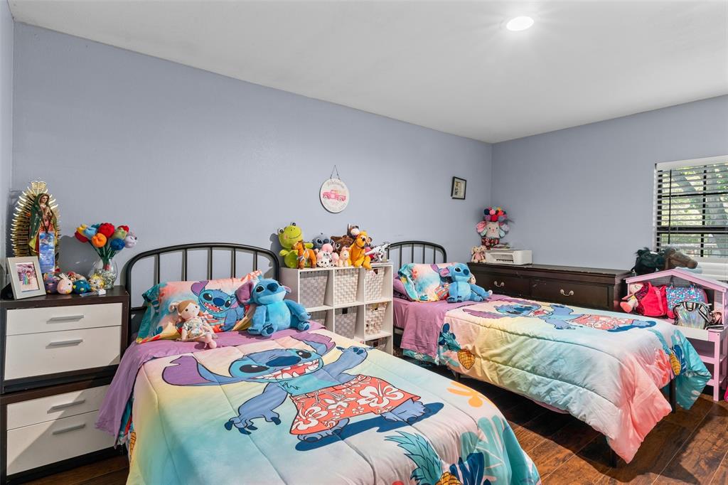 Bedroom featuring recessed ceiling lighting, a window with horizontal blinds, and wood-finish flooring