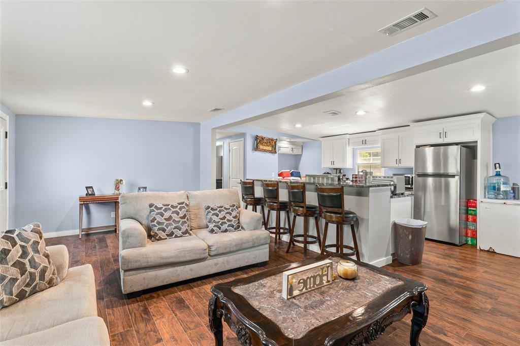 Open-concept living space featuring wood-finish flooring, recessed lighting, and kitchen cabinetry with a breakfast bar