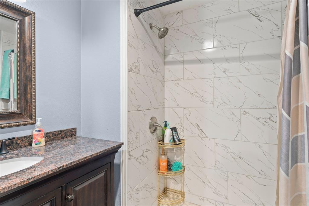 Bathroom featuring a vanity with a stone countertop and an undermount sink, paired with a shower enclosure showcasing large-format, marble-patterned tile surrounds