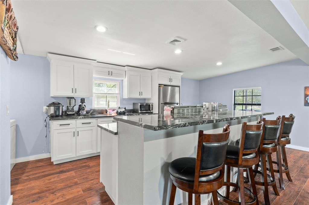 Kitchen featuring white cabinetry, stone-finish countertops, an expansive breakfast bar, recessed lighting, and wood-finish flooring