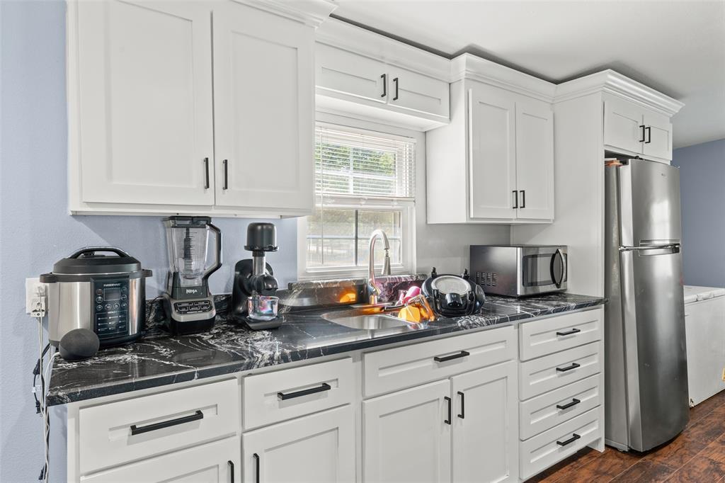 Kitchen featuring shaker-style white cabinetry, dark stone-finish countertops, stainless steel undermount sink with arched faucet, and recessed hardware