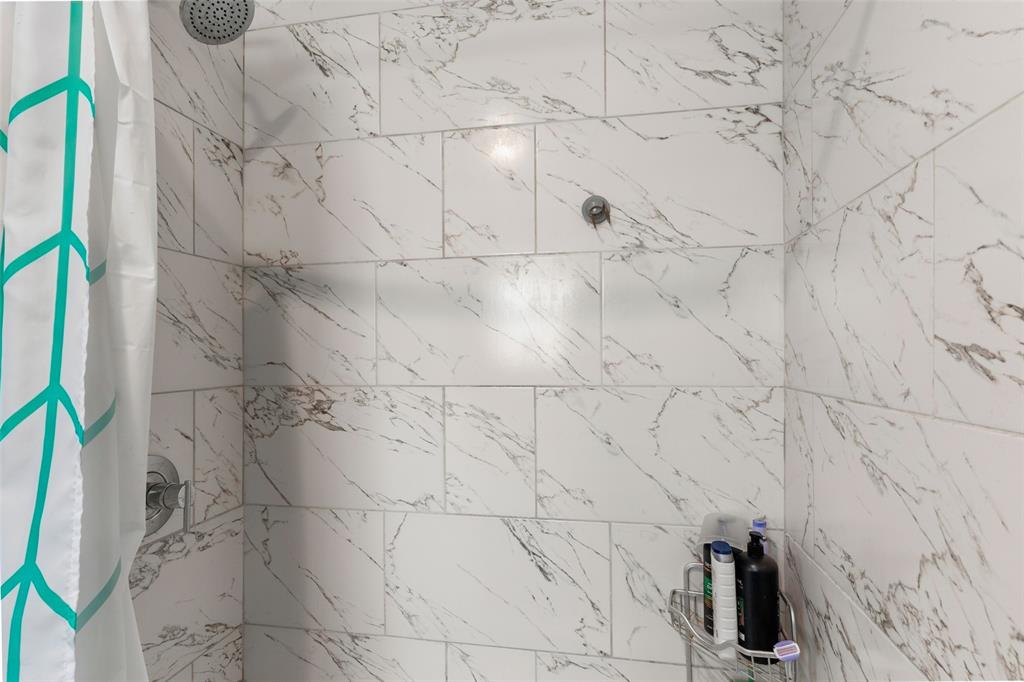 Shower enclosure featuring large-format, light-toned stone-patterned wall tile, polished chrome shower head, and matching chrome pressure-balance valve