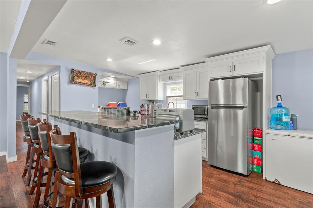 Kitchen featuring a stone-surface breakfast bar, white cabinetry, wood-finish flooring, and stainless steel refrigerator