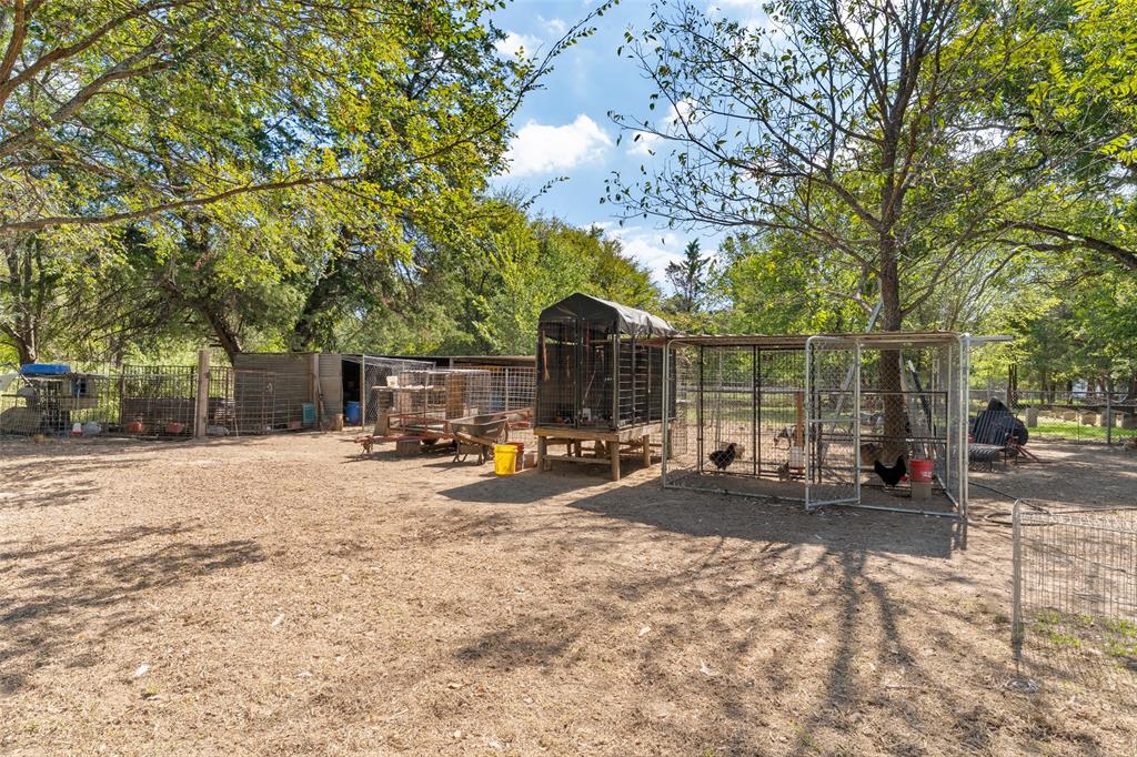 Expansive grounds featuring mature shade trees, perimeter metal fencing, and multiple external wire enclosures